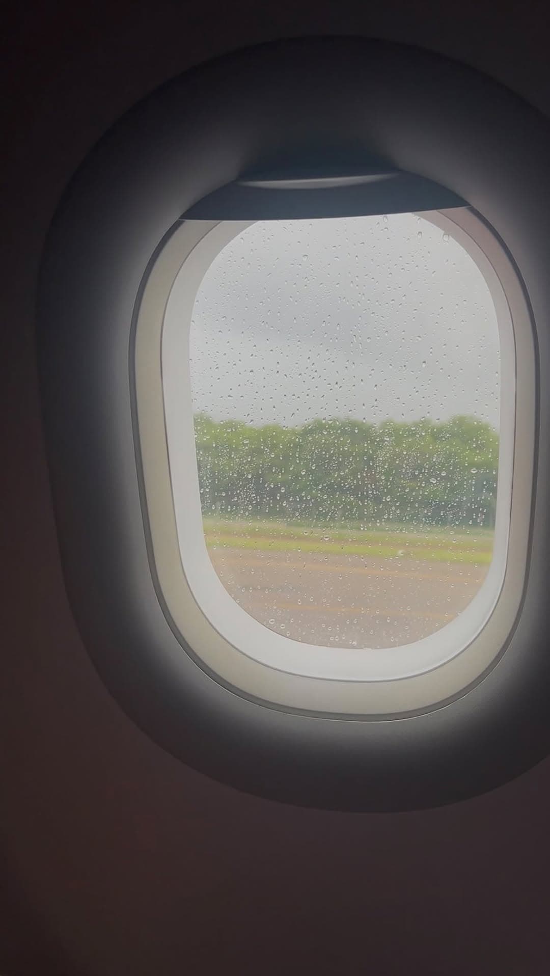 Ventanilla de avión con gotas de lluvia en la pista